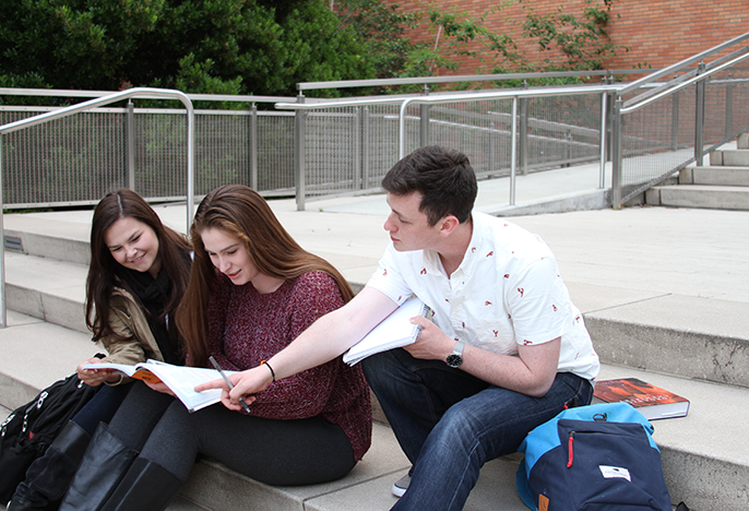Three students studying outside on the steps of Clark Library